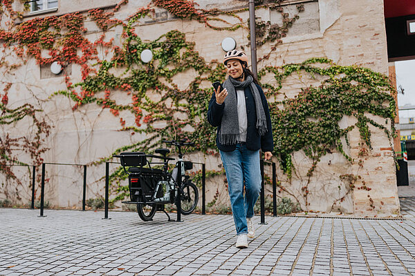 E-Bike Fahrerin mit Smartphone neben Pedelec mit Bosch-Antrieb.