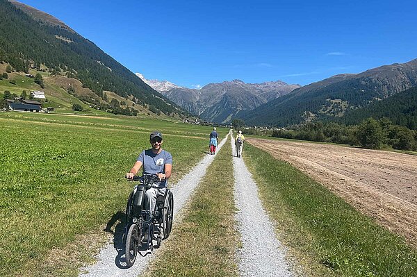 Person mit Handbike auf Kiesweg.