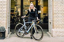 Velojournal stellt innovative Veloläden vor. Eine junge Frau mit blonden Haaren steht hinter einem Rennrad.