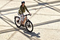 Eine Frau mit grüner Jacke fährt mit einem E-Bike über einen Platz.